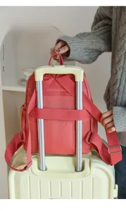 Detail of coral orange backpack with luggage strap secured on a suitcase handle