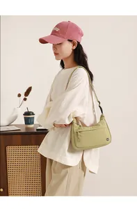 Close-up of a light green nylon dumpling bag with adjustable strap in a cozy setting