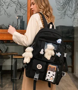 Detalle de mochila de lona negra con osito de peluche, insignias y diseño de múltiples bolsillos