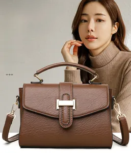 Detail of brown textured leather handbag featuring golden square lock and detachable strap