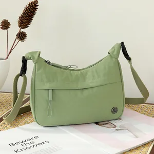 Sage green nylon crossbody bag with adjustable strap and metal logo on a woven mat