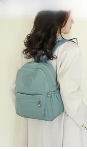 Rear view of a light green nylon backpack on a model showing size and travel fit