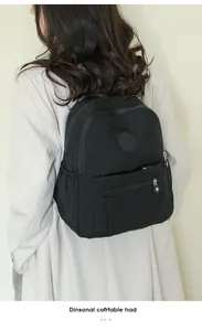 Side view of black oxford fabric backpack worn by model, showing layered zipper compartments