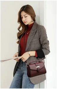 Detail of burgundy pebbled leather handbag with gold metal clasp on a stylish model