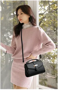 Detail of black pebbled leather handbag with gold metal clasp and adjustable shoulder strap