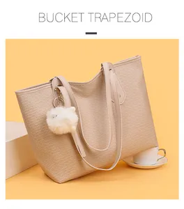 Detail of beige trapezoid tote bag with woven texture and white plush charm on yellow background