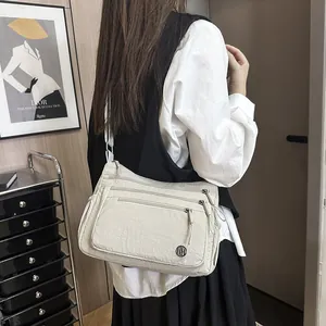 Sac bandoulière en nylon beige avec plusieurs poches zippées porté par un mannequin