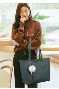 Detailed close-up of dark green woven tote bag featuring a soft white plush ball charm