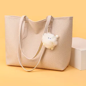 Minimalist beige woven tote bag with leather straps and plush charm on yellow background