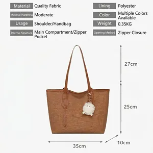 Brown woven tote bag with a white fur ball pendant and top zipper closure