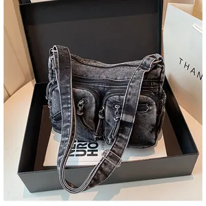 Détail du sac bandoulière en denim délavé gris avec poches zippées dans une boîte