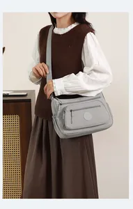 Side view of grey nylon crossbody bag with multiple zippers worn by a female model