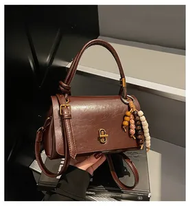 Detail der braunen Vintage-Handtasche mit Knotengriff und Perlenanhänger auf der Treppe