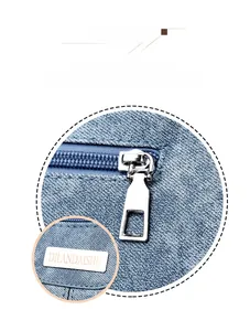 Macro detail of silver zipper and brand metal plate on blue textured leather crossbody bag