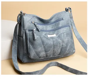 Detail view of the gray-blue crossbody bag with double front zippers and metal nameplate