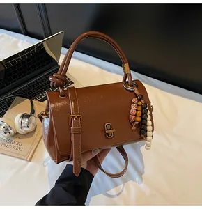 Nahaufnahme der karamellbraunen Ledertasche mit Retro-Drehverschluss und Perlenanhänger