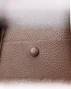 Close-up of brown litchi grain leather texture and decorative round button on tote bag