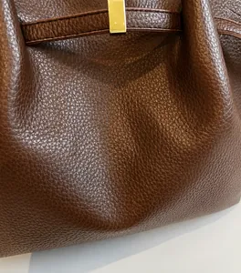 Detail of dark brown tote bag showing pebbled leather texture and golden metal buckle