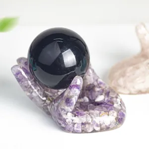 Sphère d'obsidienne polie avec base décorative en résine et cristaux violets en main