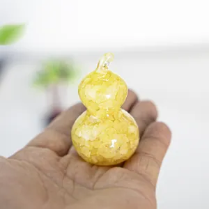Detailed close-up of a hand holding a small yellow resin gourd with natural citrine stones