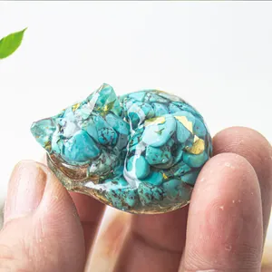Handheld view of a small sleeping cat statue with turquoise stone and gold foil flakes