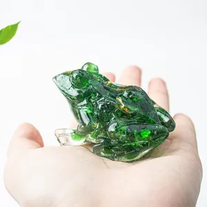 Macro shot of a small green crystal frog resin figurine with gold leaf inside on a palm