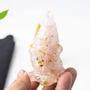 Hand holding a translucent pink crystal gnome figurine with gold leaf decorative flakes