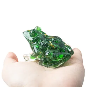 Cute green crystal frog figurine with gold foil flakes displayed on a person's hand