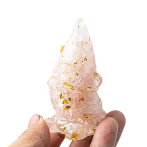 Pink crystal gnome figurine with gold foil flakes held in hand on white background