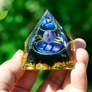 Close-up of Gemini Orgone pyramid with purple crystal ball and gold foil in hand