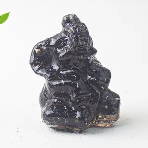 Polished black obsidian elephant figurine with raised trunk on white stone surface