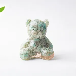 Dettaglio ravvicinato di una statuetta a orso in resina con cristalli verdi e base oro