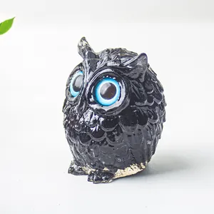 Détail d'une figurine de hibou en résine noire avec yeux bleus et texture écaillée