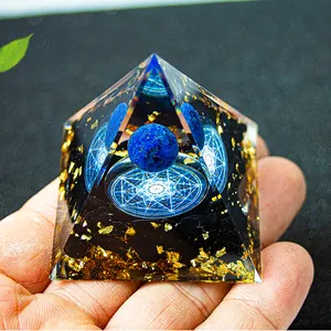 Nahaufnahme der Orgonit-Pyramide mit blauer Kristallkugel und Blattgold in der Hand