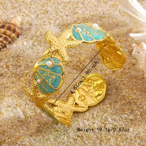 Gouden armband met zeester, schelp en parels gepresenteerd op een zandige achtergrond