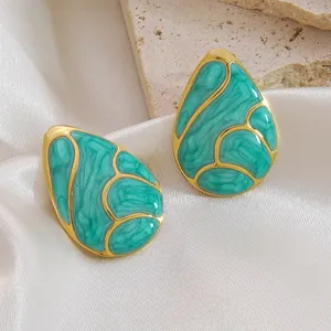 Macro shot of gold teardrop earrings with green marble texture on a satin backdrop