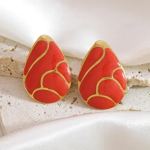 Macro shot of red enamel teardrop earrings with gold metal frame on a marble texture