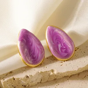 Gros plan de boucles d'oreilles goutte dorées avec émail marbré violet sur soie