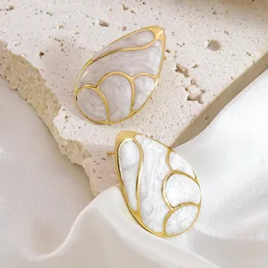 Macro view of gold teardrop earrings with white marble texture on stone and satin