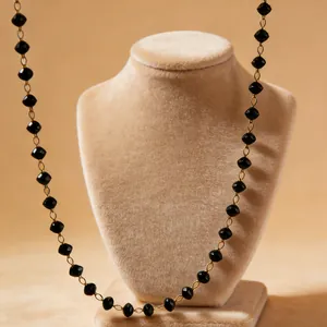Detail of bohemian black beaded necklace with gold links on a velvet jewelry display stand