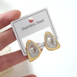 Detail of stainless steel earrings with gold frame and marble inlay on a display card