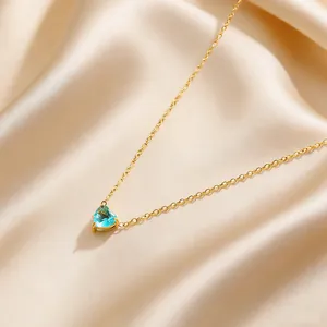 Close-up of golden heart necklace with light blue gemstone on silky champagne fabric