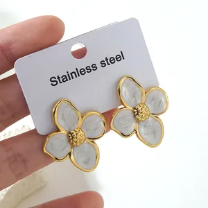 Close-up of white enamel flower earrings with gold edges on a stainless steel card