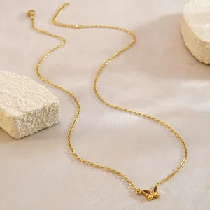Collana a farfalla dorata con cristalli rossi e blu su superficie beige