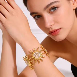 Detailed close-up of golden sun-shaped bracelet with white enamel spiral on model wrist