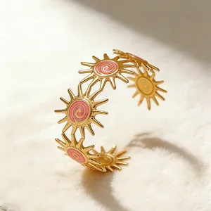 Detail of gold sunburst cuff bracelet with pink enamel spiral and radiant sun design