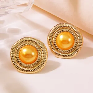 Nahaufnahme von Vintage-Knopfohrringen in Gold mit Sonnenstrahl-Textur und oranger Perle