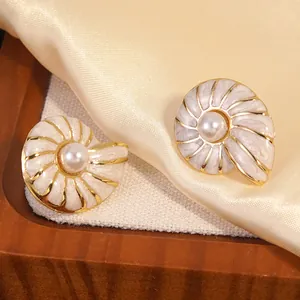 Detailed macro shot of nautilus-shaped pearl earrings with cream enamel and gold accents