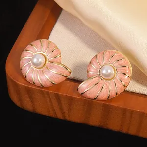 Detailed view of pink enamel shell earrings with gold plating and pearl inlay on satin