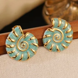 Detailed close-up of golden conch earrings with mint green marble enamel on wood